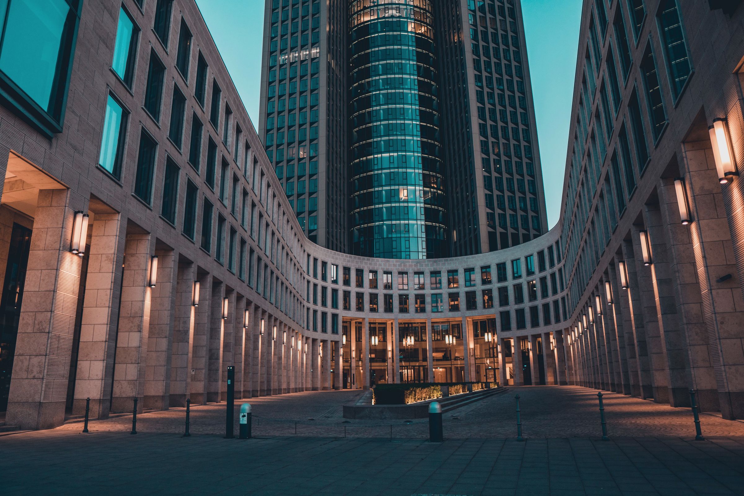 An office campus courtyard at blue hour, colonnade lamps lit